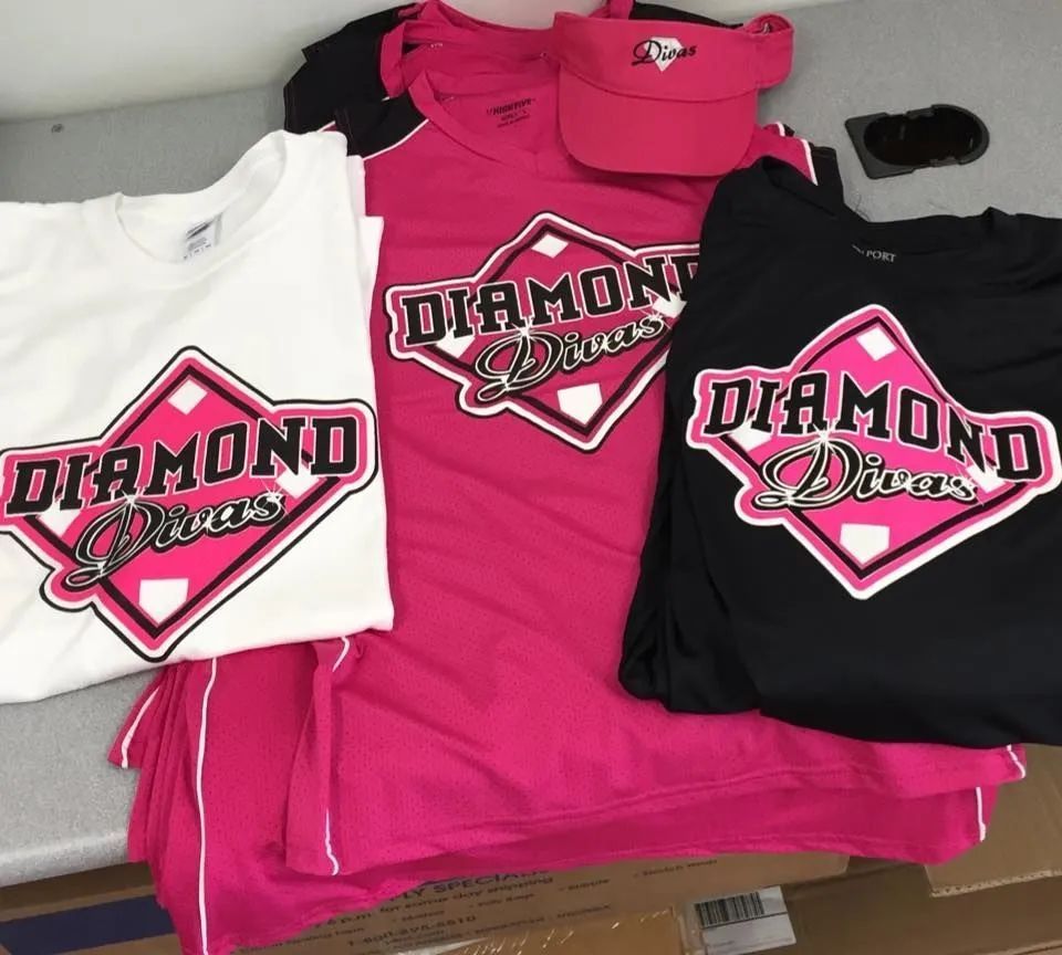 Three Diamond Diva shirts in white, pink, and black laid out on a table.