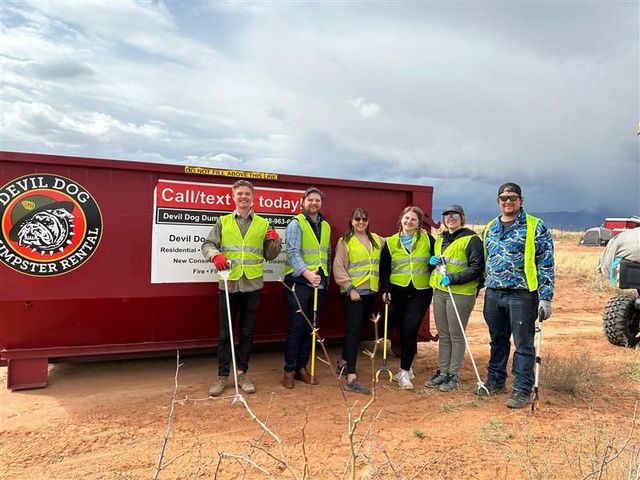A group of people are standing in front of a red dumpster.