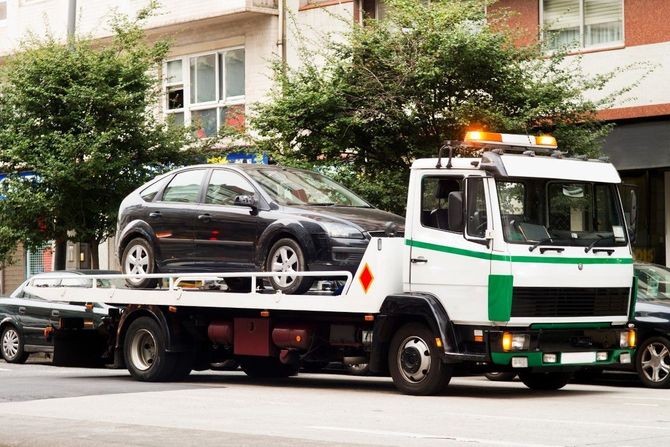 Tow truck loading a black car on a flatbed in a city street