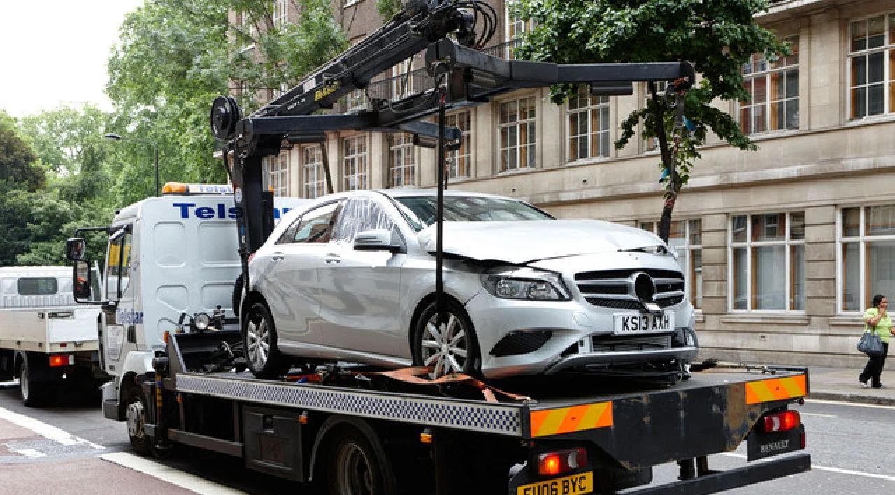 Silver Mercedes on a tow truck in front of a building, with another vehicle behind it.