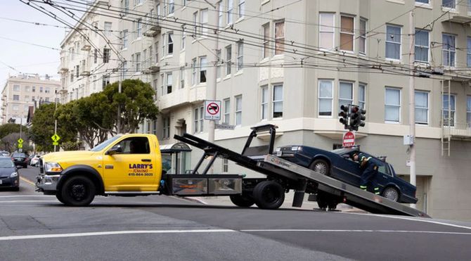 Yellow tow truck loading a black sedan on a flatbed in a city street