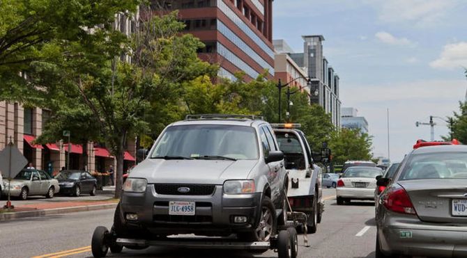 Urban street with cars in traffic beside buildings and trees on a sunny day
