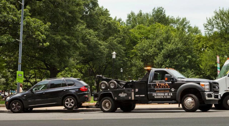 Tow truck towing a black SUV on a tree-lined street with a traffic sign in the background