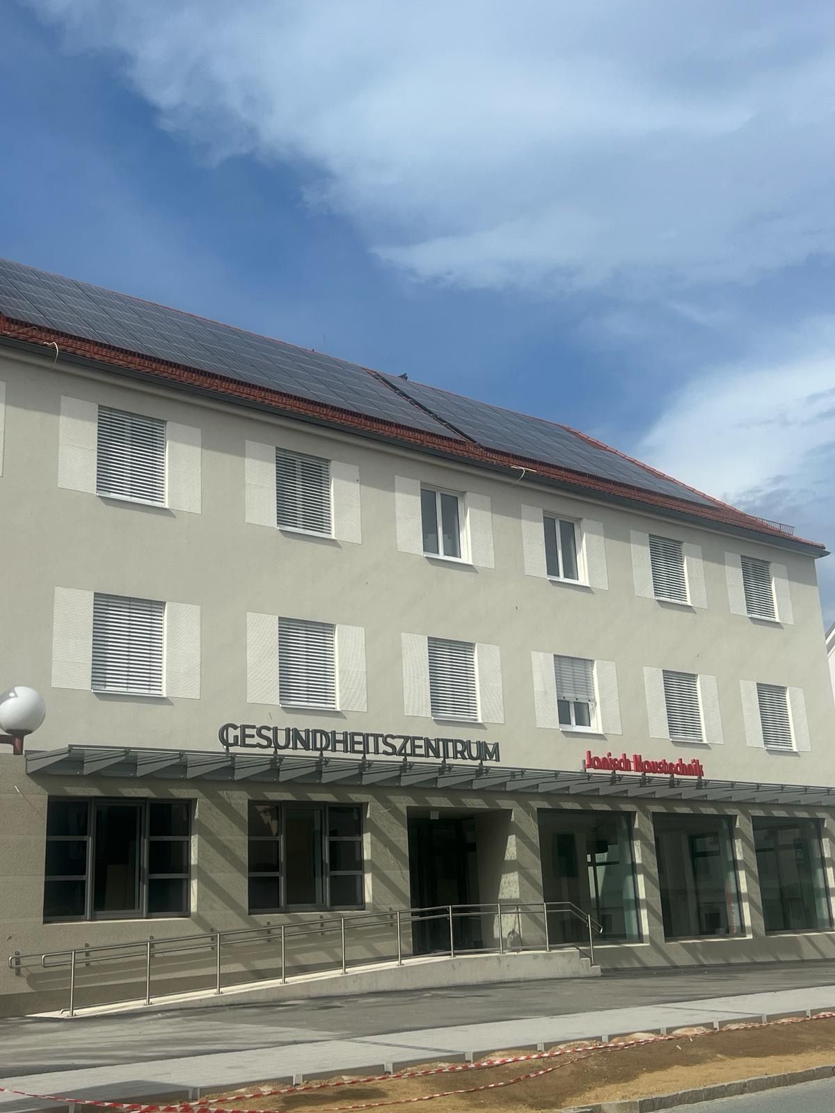 Physiotherapieraum mit Untersuchungstisch, Schreibtisch, anatomischen Diagrammen und zwei grünen Stühlen.