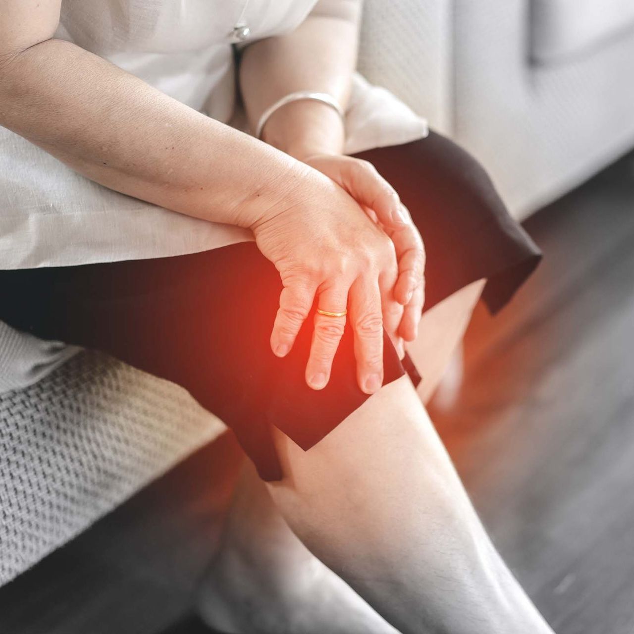 Frau mit den Händen auf dem Knie, durch rotes Leuchten als Schmerzstelle gekennzeichnet.