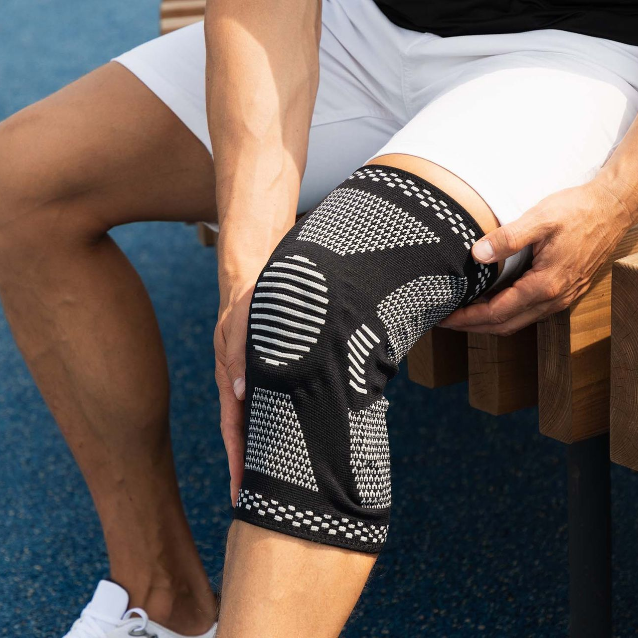 Person mit einer schwarzen Knieorthese am Knie, die im Freien sitzt.