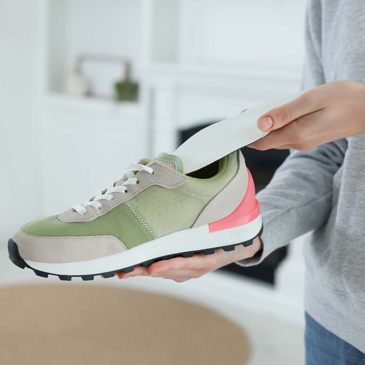 Eine Person legt im Innenbereich eine desodorierende Einlage in einen grün-beigen-rosa Sneaker ein.