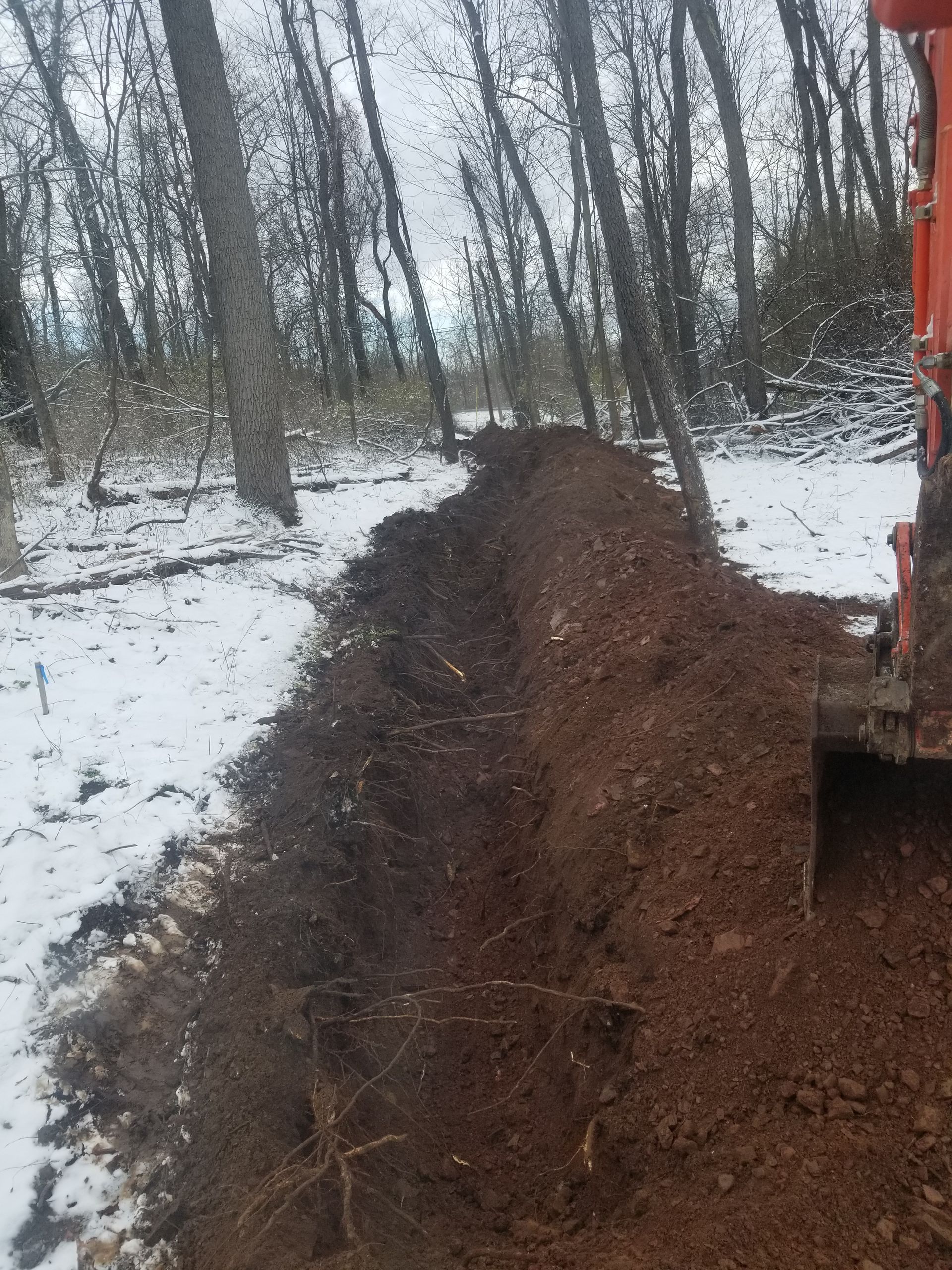 An excavator is digging a trench in the snow