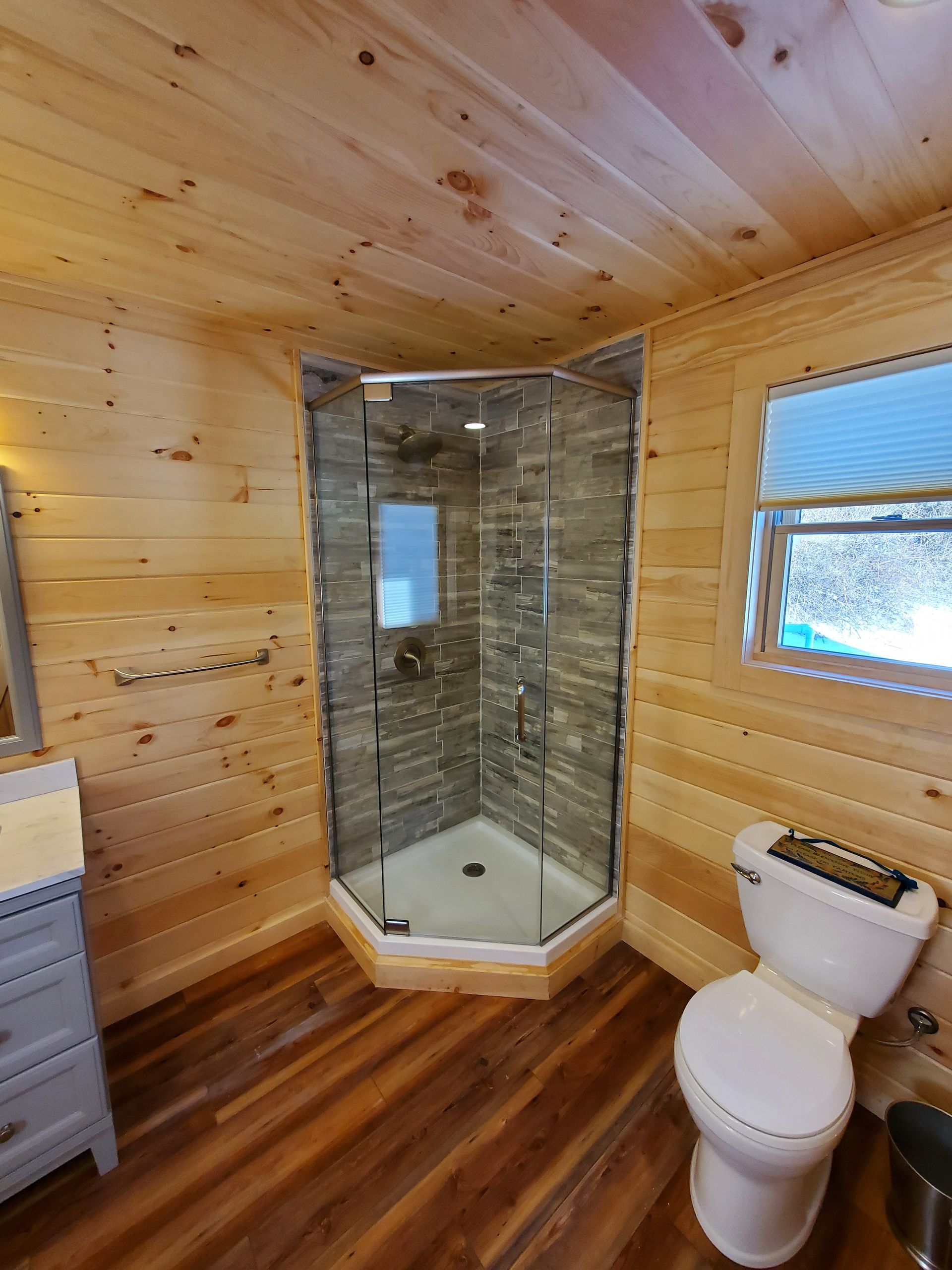 A bathroom with a toilet , sink , shower and window.