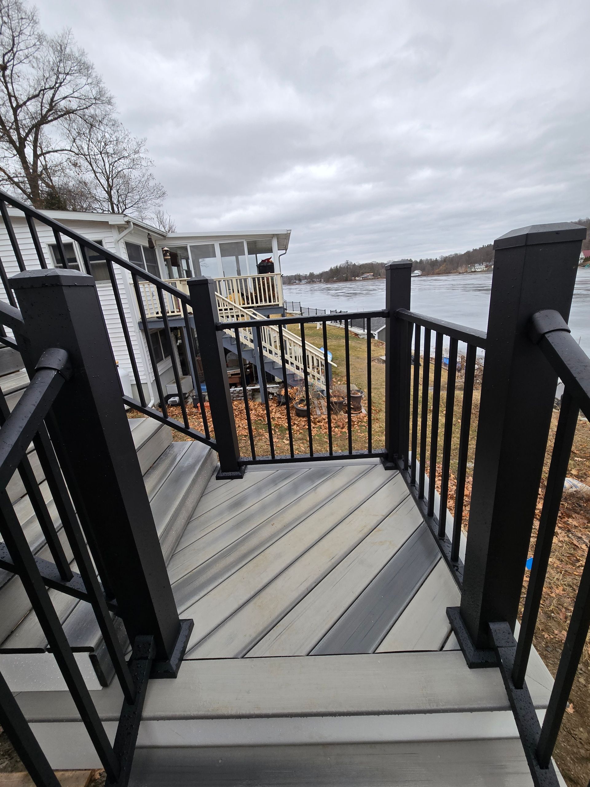 A staircase leading up to a deck with a black railing and a house in the background.