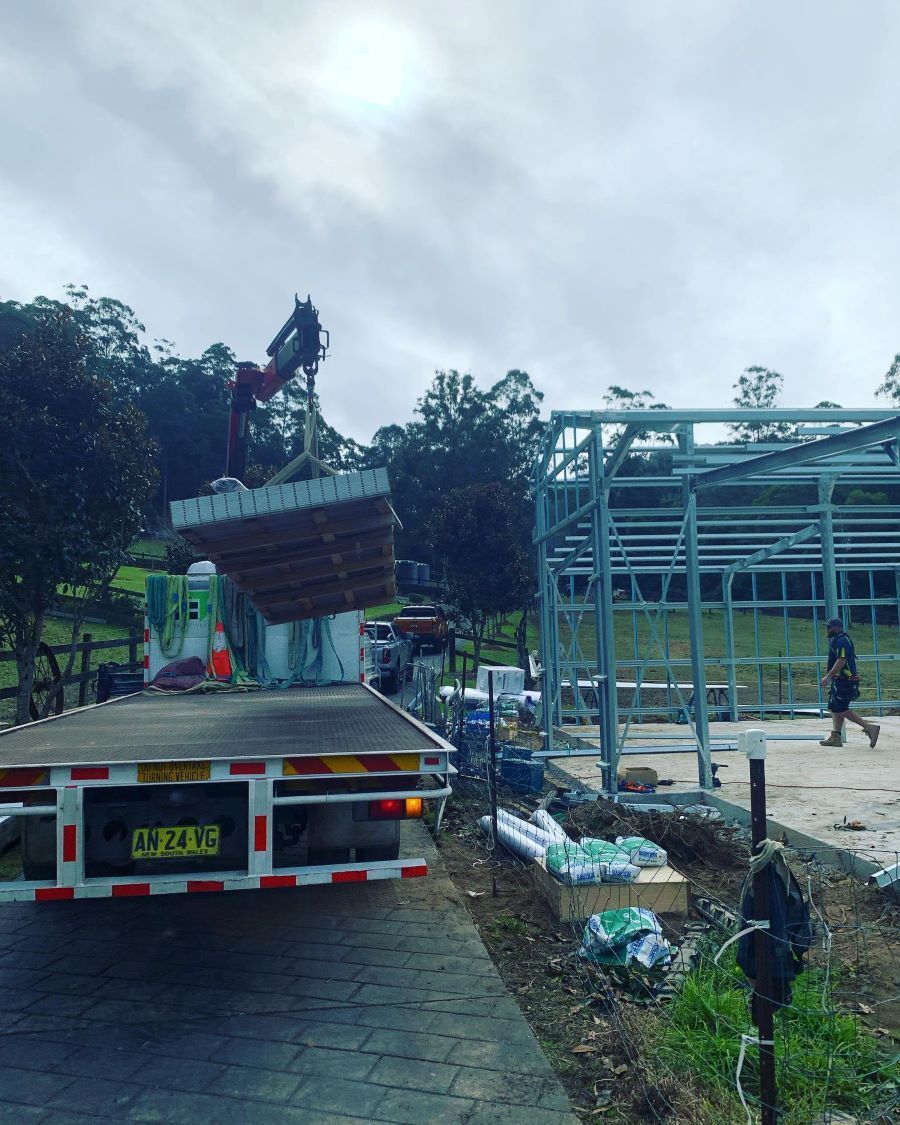 A Crane Lifts a Stack of Concrete Slabs from A Flatbed Truck — Express Timber Solutions In Long Jetty, NSW