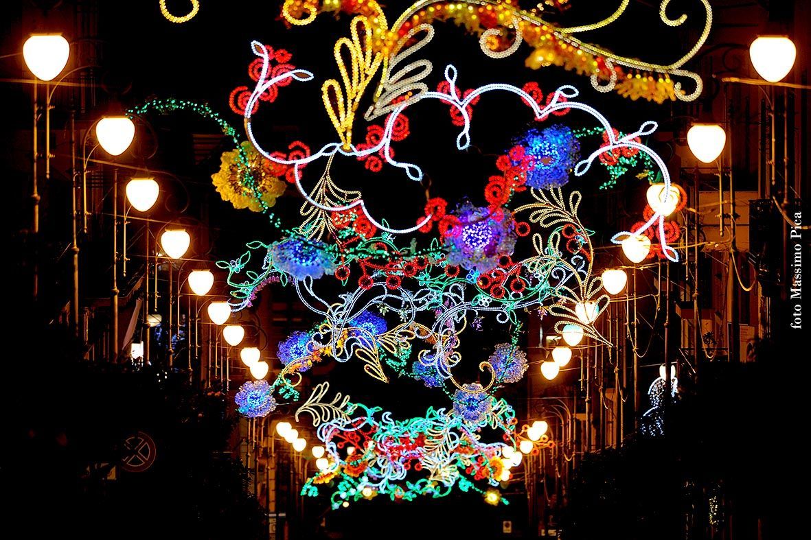 Una colorata installazione luminosa a forma di cuore risplende su una strada buia fiancheggiata da lampioni.