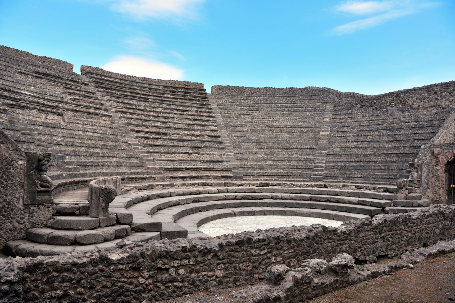 Antico anfiteatro in pietra con posti a sedere semicircolari sotto un cielo azzurro.