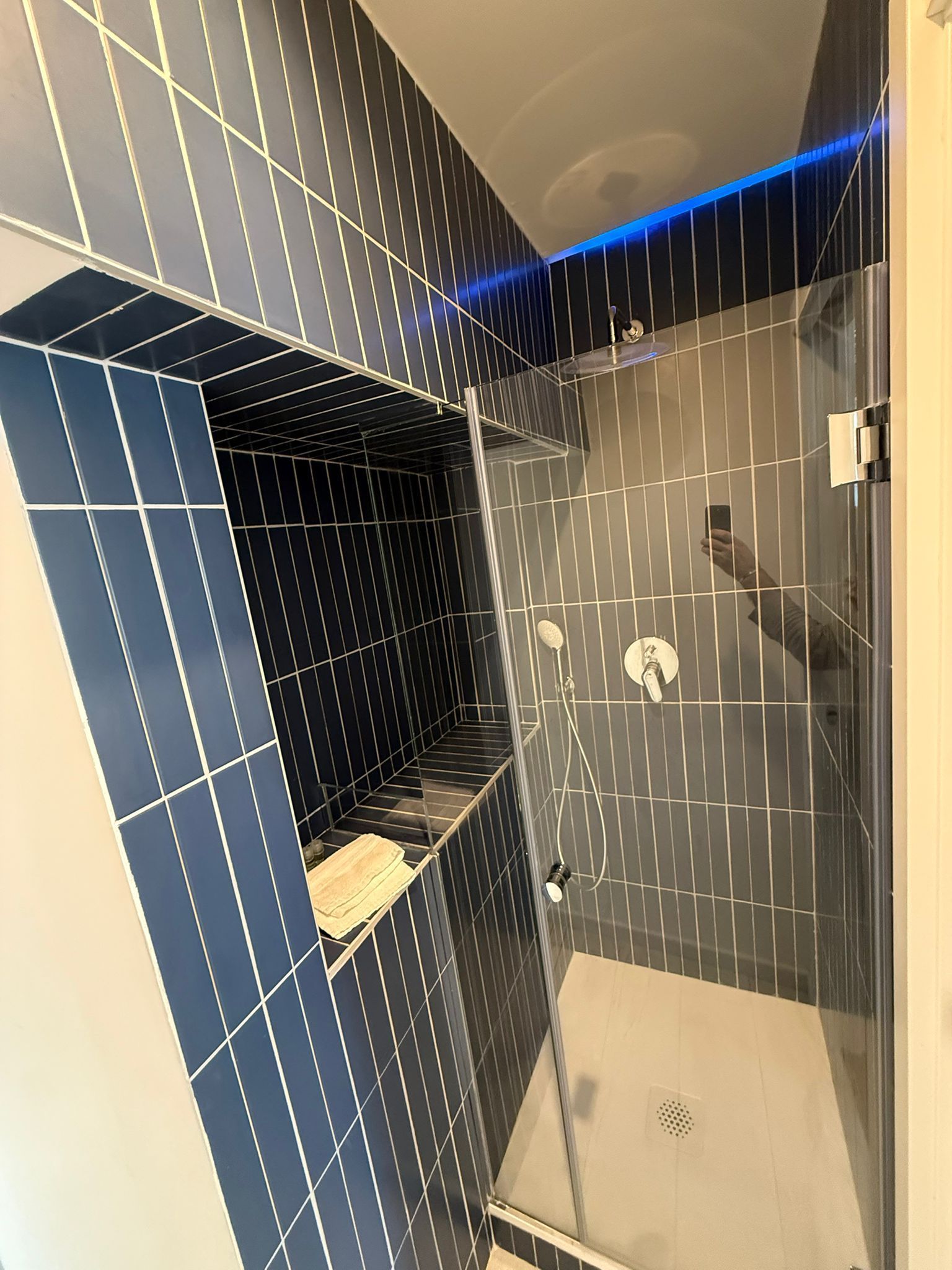 Doccia moderna con pareti rivestite di piastrelle blu scuro, porta in vetro e illuminazione a LED blu.