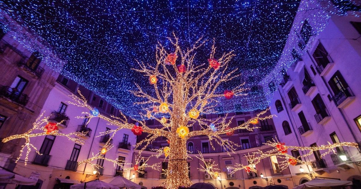 Un cortile festivo con un albero illuminato, luci scintillanti e luci che sembrano coriandoli sopra la testa durante la notte.