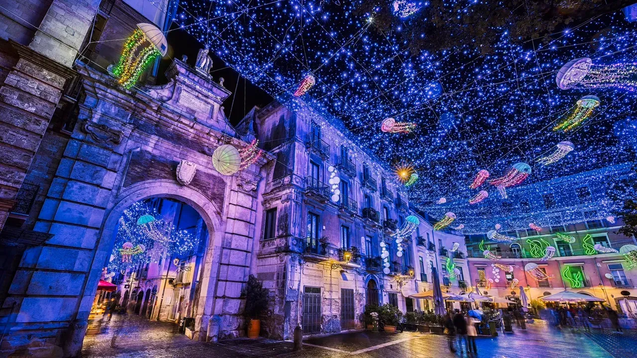 Paesaggio urbano notturno dai colori vivaci, con edifici storici illuminati e uno spettacolo di luci stellate nel cielo.