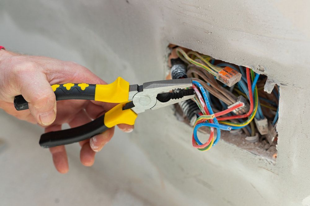 A Person Is Using Pliers To Fix An Electrical Outlet — Robon Electrical In Cairns, QLD