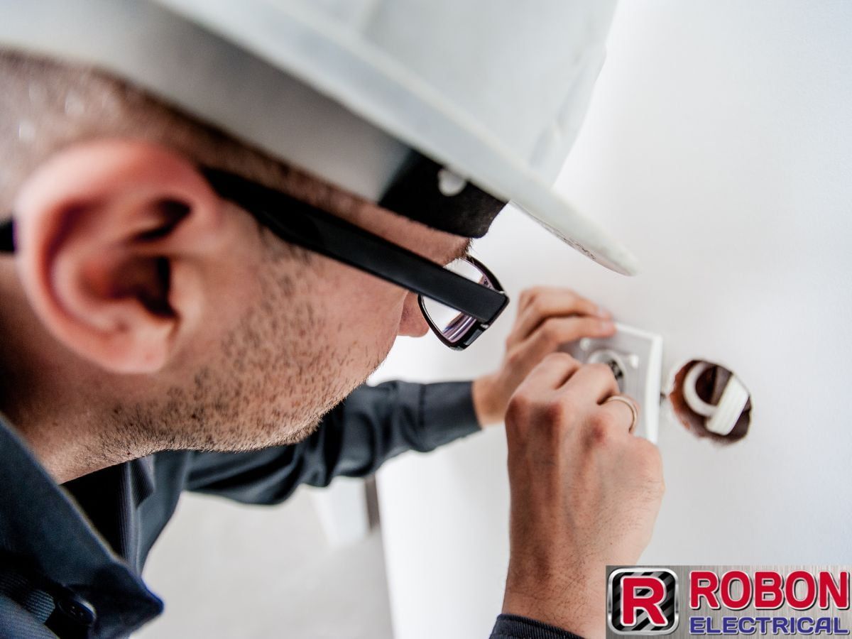 A Man Wearing A Hard Hat Is Working On An Electrical Outlet — Robon Electrical In Holloways Beach, QLD