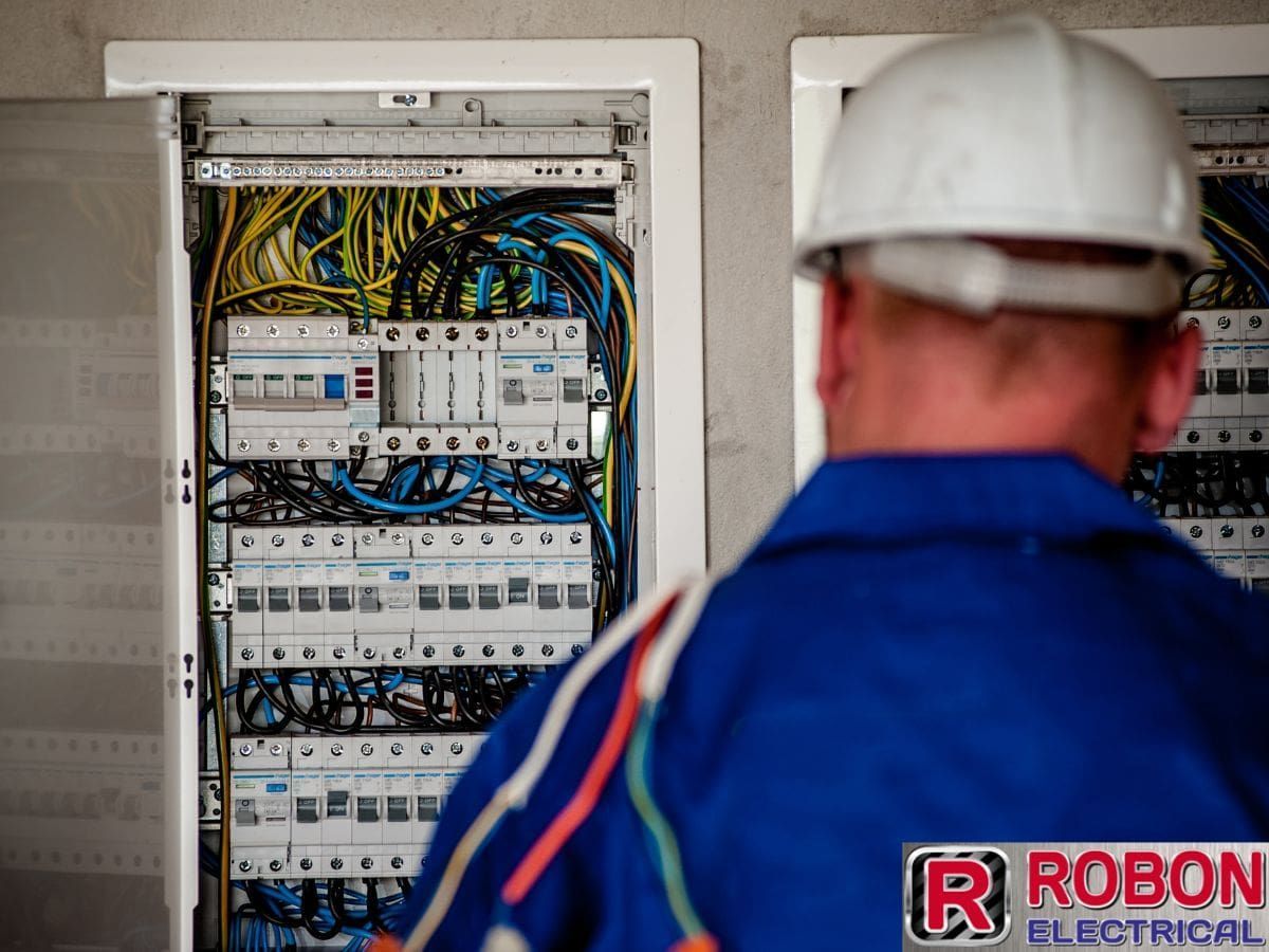 A Man Wearing A Hard Hat Is Looking At An Electrical Box — Robon Electrical In Holloways Beach, QLD