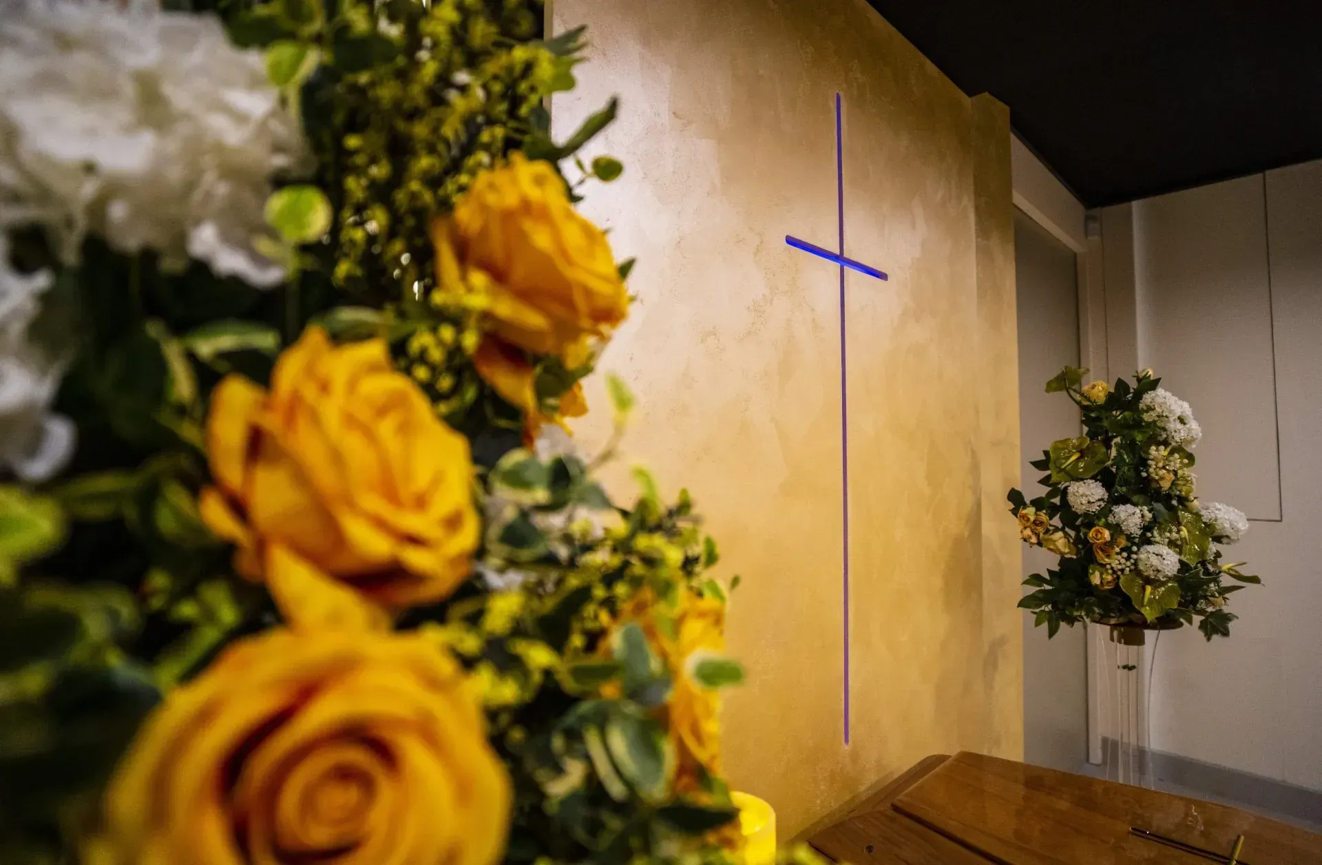 Sullo sfondo c'è una croce sul muro e in primo piano ci sono dei fiori.