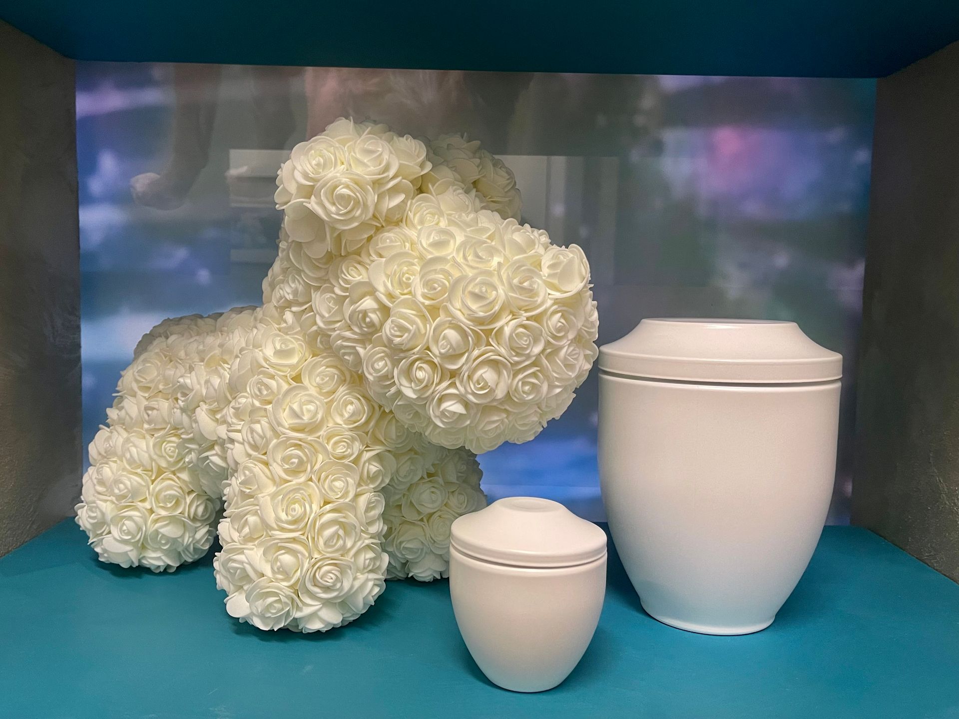 Un cane di peluche fatto di rose bianche è seduto accanto a un'urna bianca.