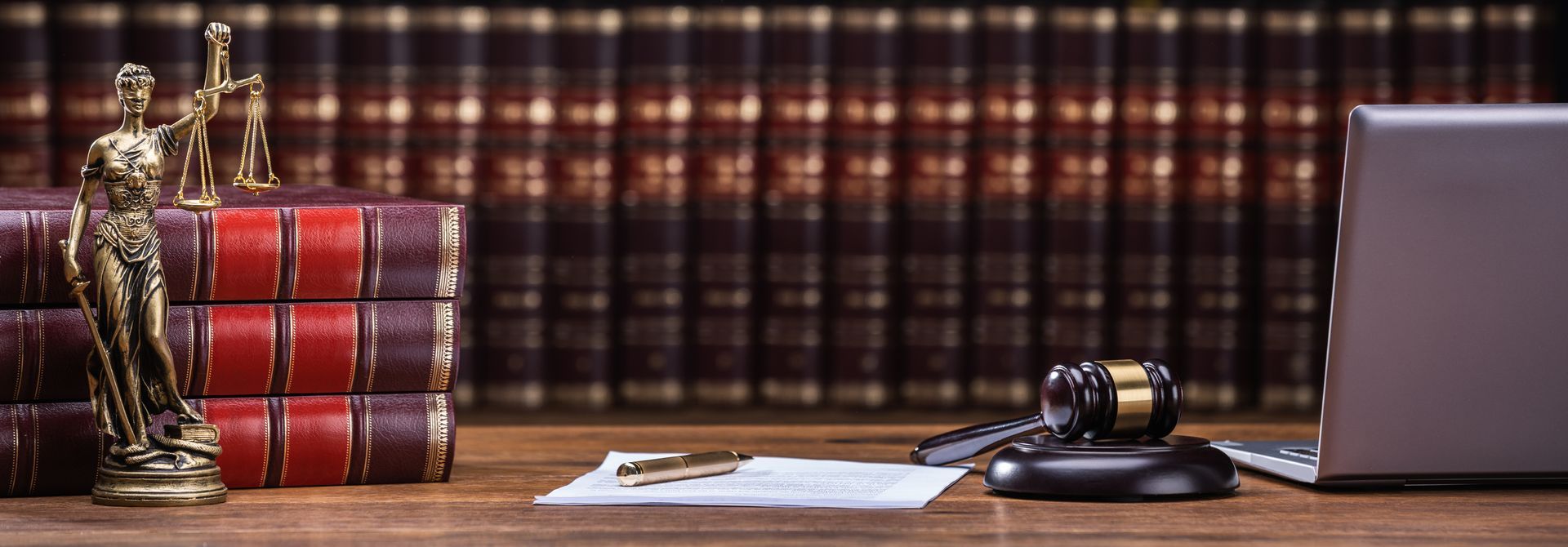 A desk with books, a scale statue, a gavel, and a laptop, suggesting a legal setting.