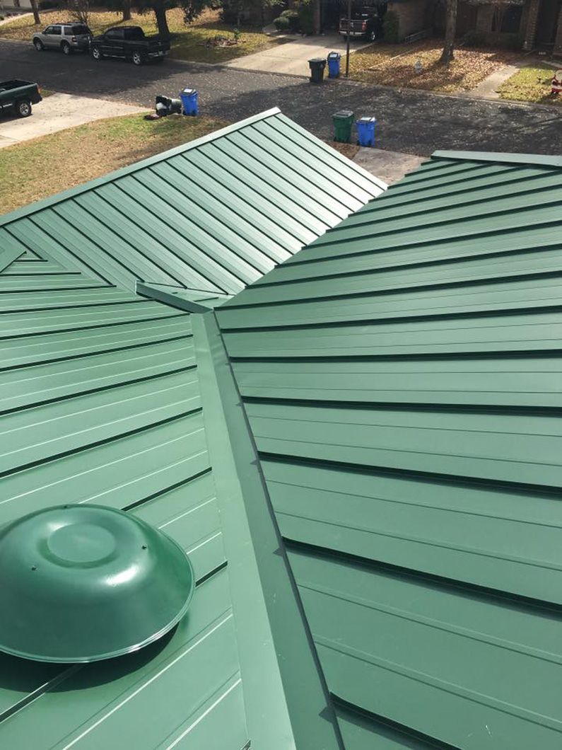 Green metal roof with ridge cap and vent, overlooking a parking area.