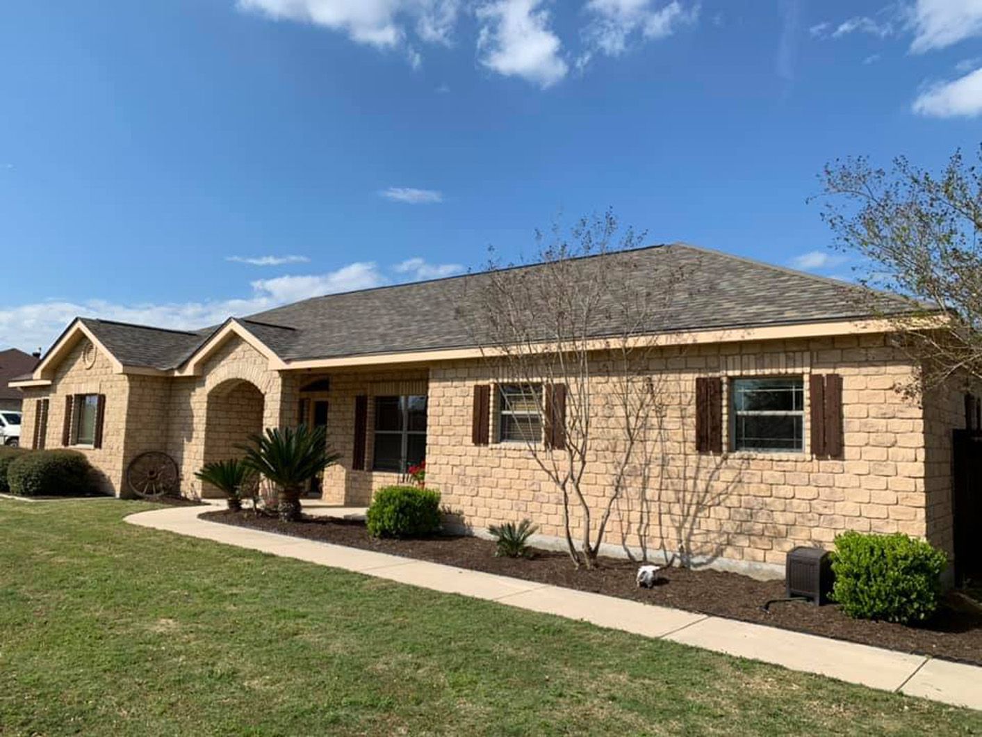 Beige brick house with brown shutters and a walkway, under a blue sky.