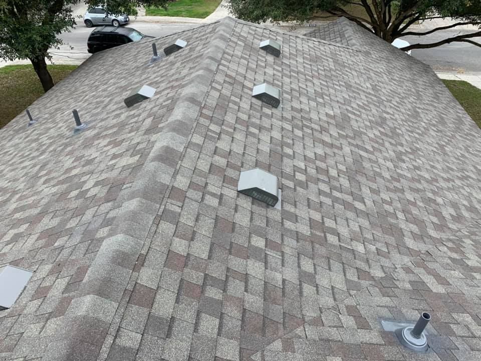 Overhead view of a house roof with brown asphalt shingles and several vents.
