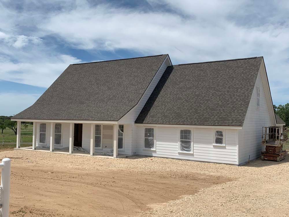 White house under construction with brown roof on a gravel lot under a cloudy sky.
