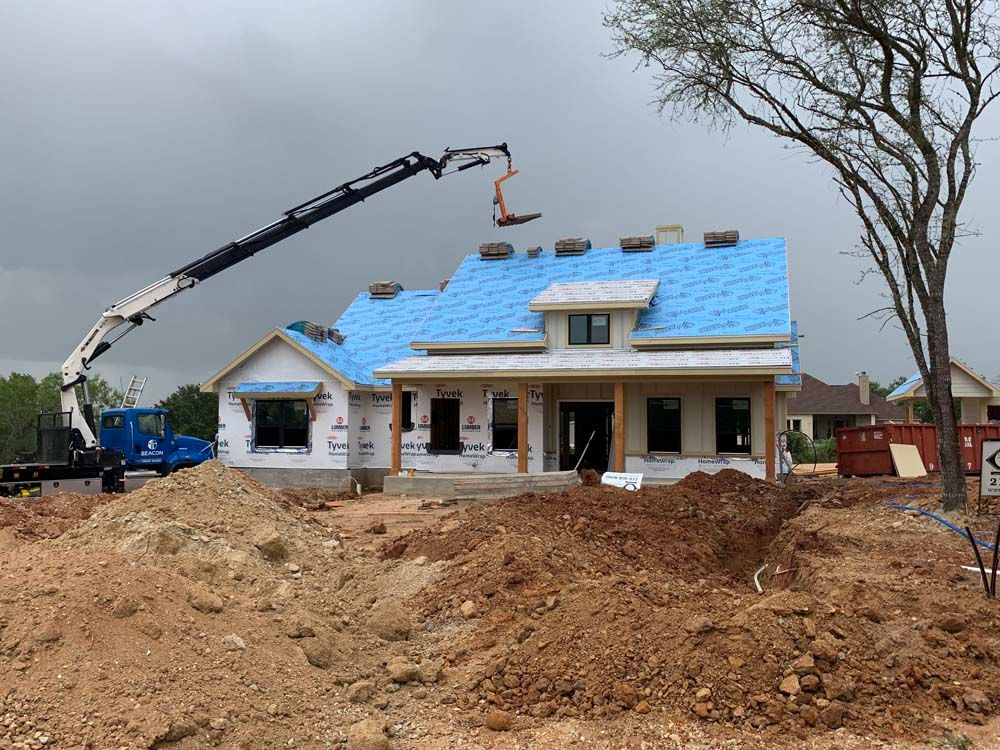 Construction of a house with a crane placing roof materials. Cloudy day, dirt pile in foreground.