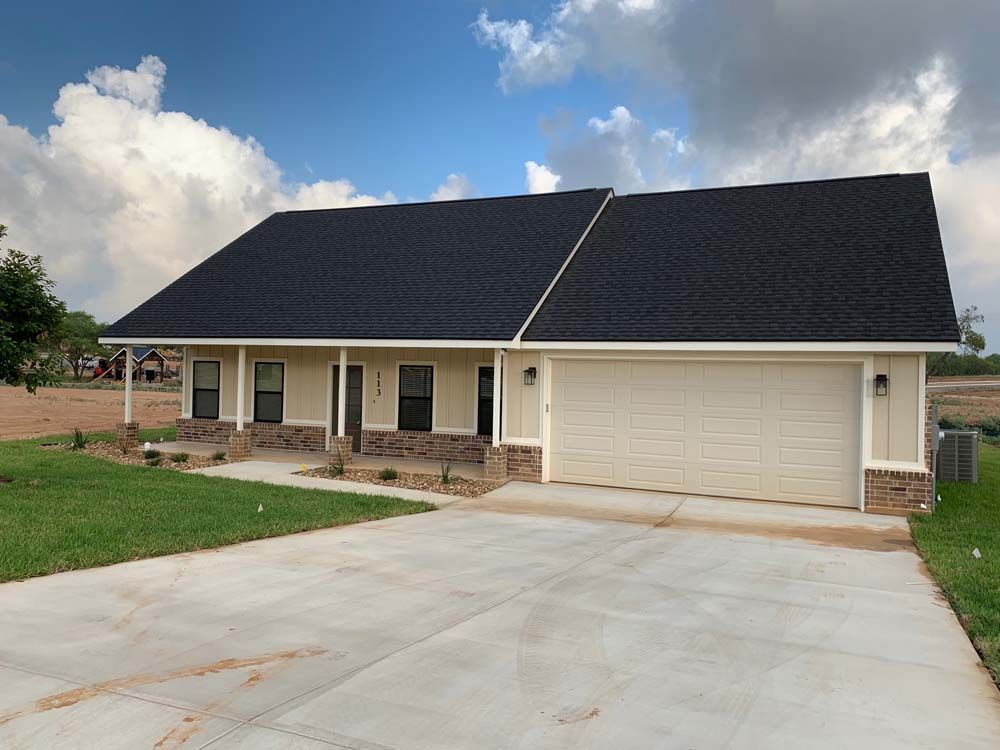 Beige house with black roof, garage, and driveway on a sunny day.