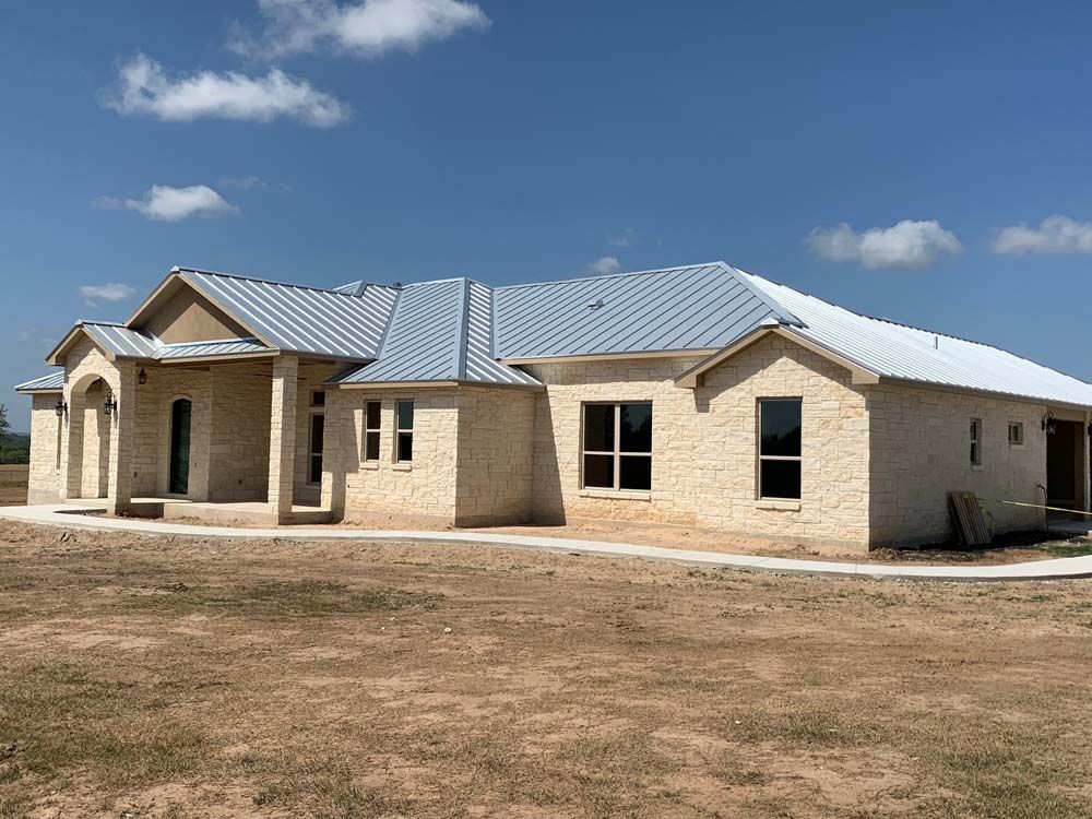 A light-colored brick house under construction with a metal roof on a sunny day.