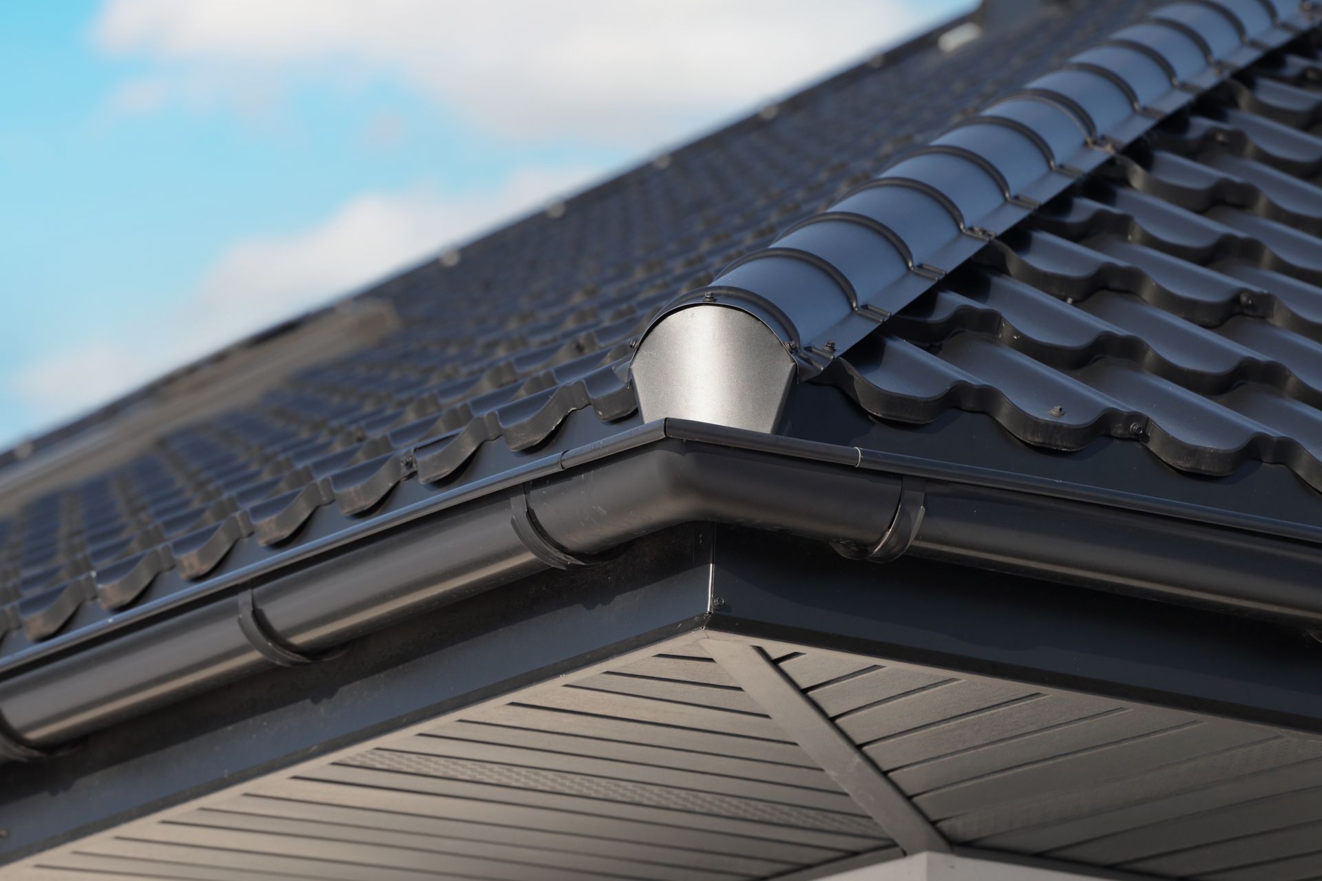 Black roof with gutters and a downspout, against a blue sky.