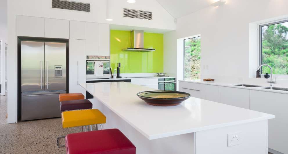A kitchen with white cabinets , stools , a refrigerator and a bowl on the counter.
