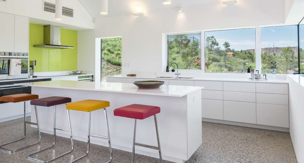 A kitchen with white cabinets , a large island , and colorful bar stools.