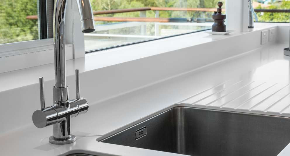 A kitchen sink with a faucet and a window in the background.