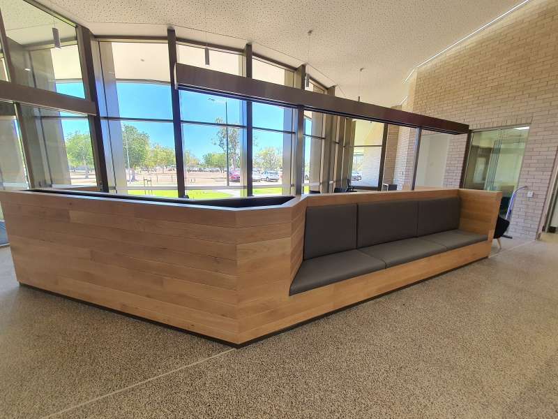 A long wooden couch in a lobby with a lot of windows.