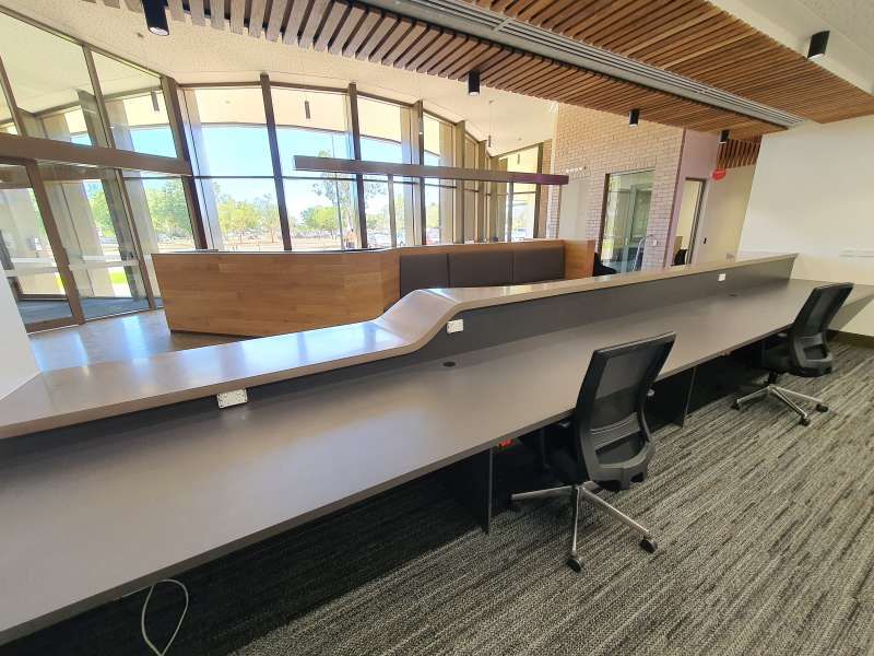 A long desk with two chairs in a room with a lot of windows.
