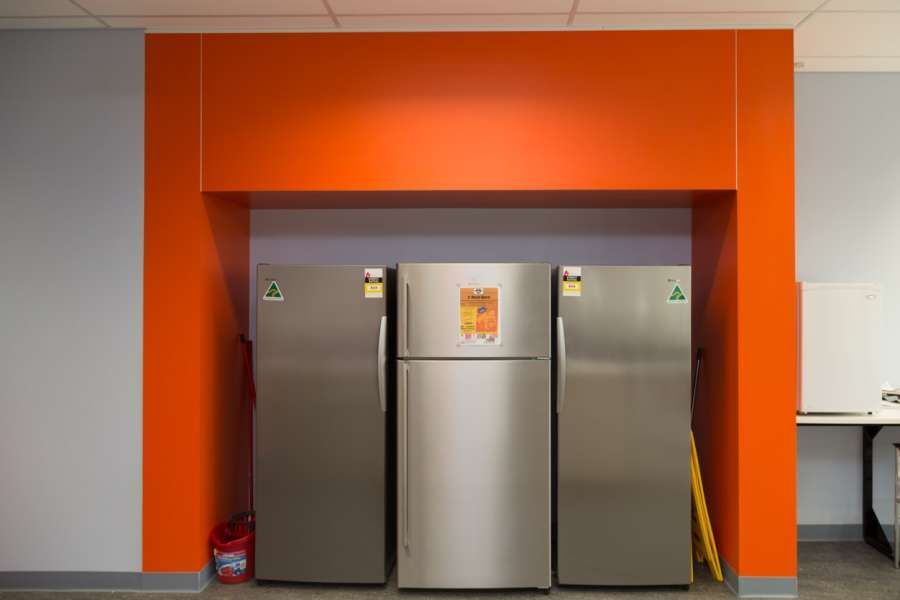 Three refrigerators are lined up in a room with orange walls.