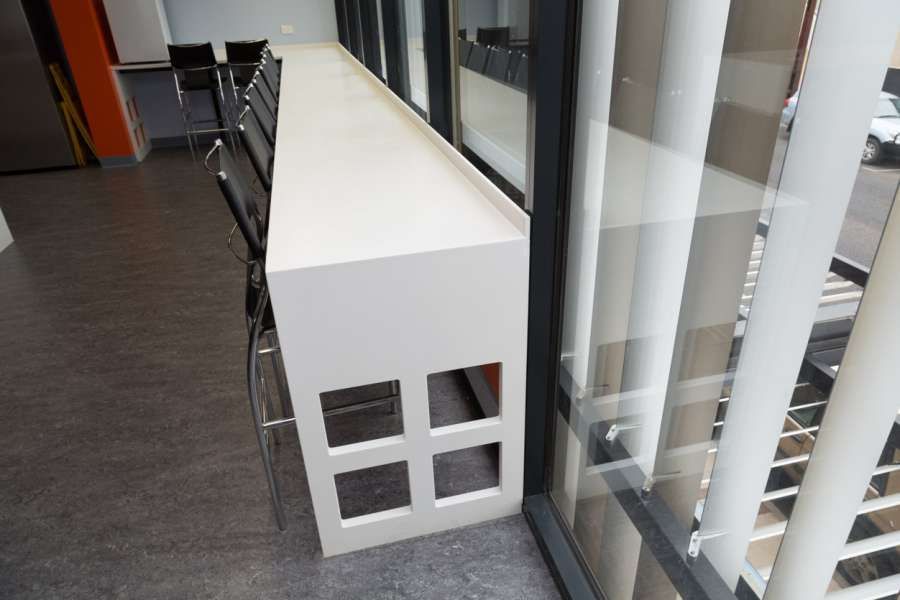 A long white table is sitting next to a window in a room.