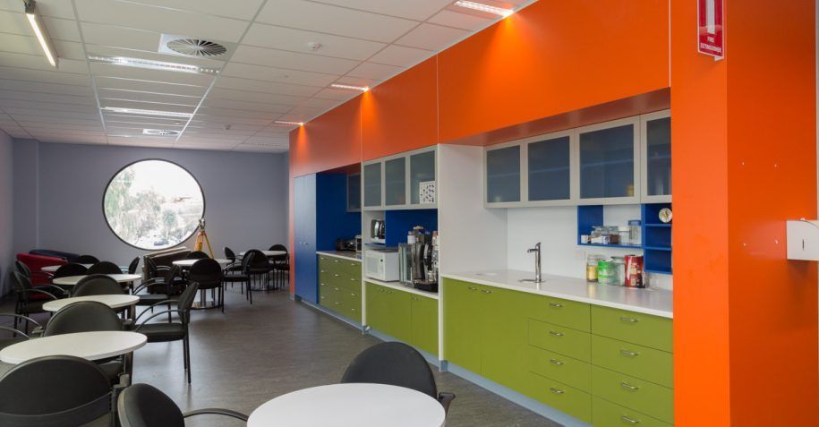 A room with orange walls , green cabinets , tables and chairs.