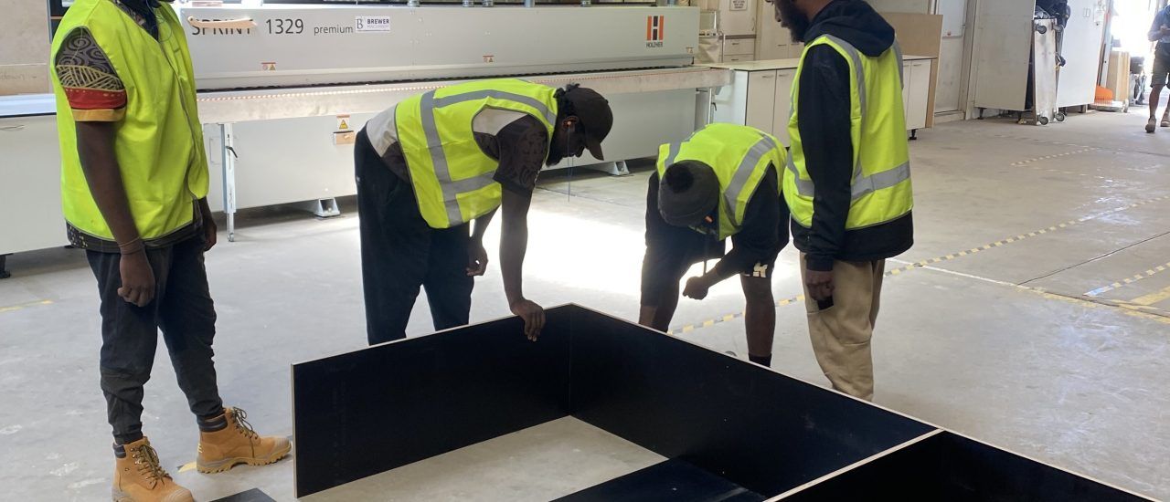 A group of men are working on a piece of wood in a factory.
