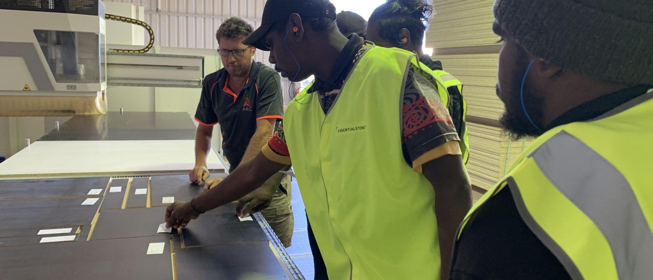 A group of men in yellow vests are standing around a table.