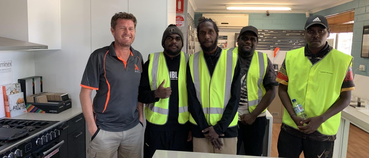 A group of men in yellow vests are standing next to each other in a kitchen.