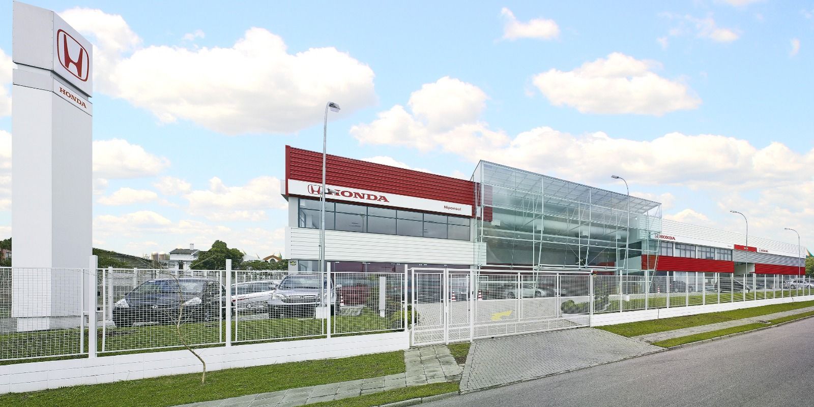 Honda dealership exterior with tall sign and parked cars under a blue sky
