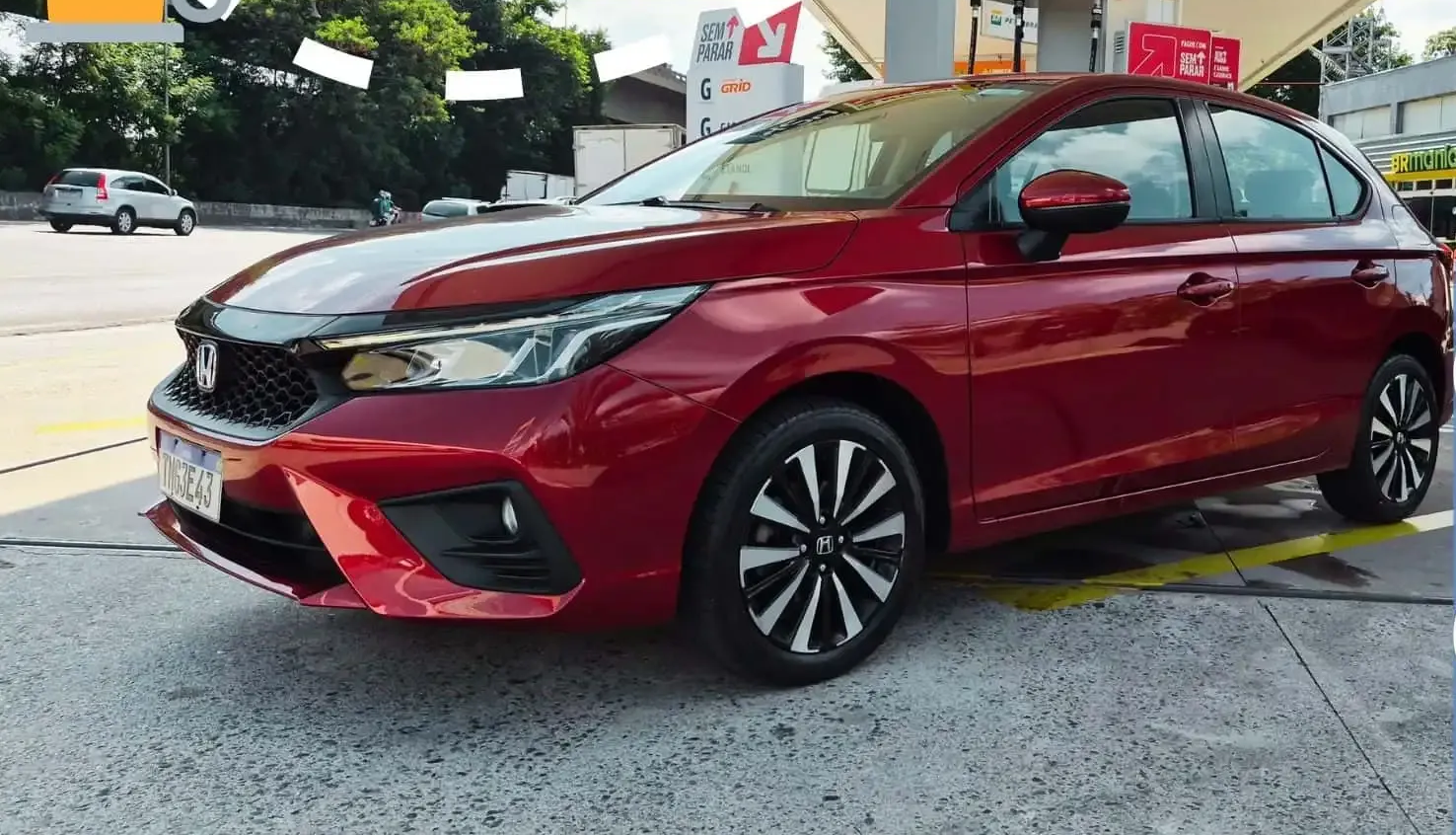 Carro hatchback vermelho estacionado em uma bomba de gasolina, visto da frente, do lado esquerdo.