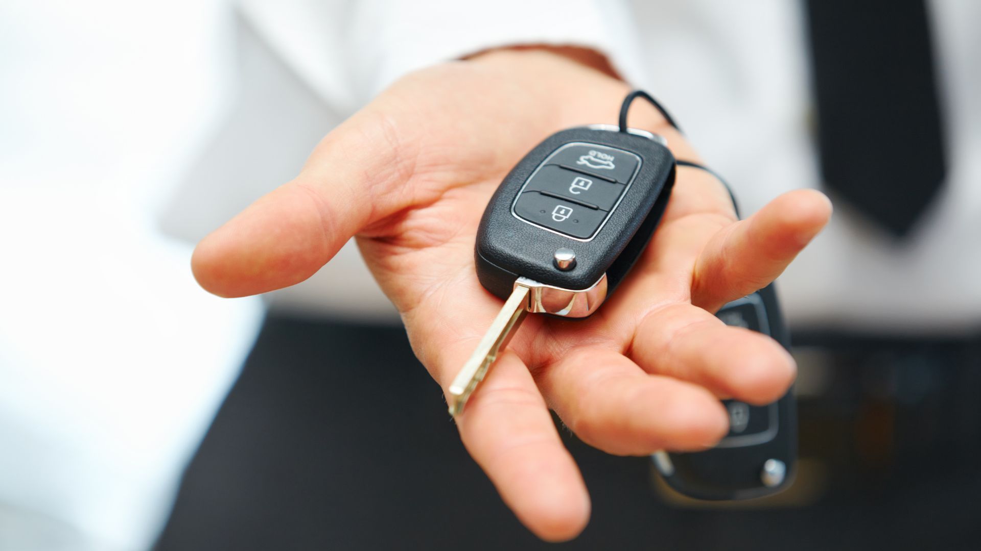 Hand holding a car key fob with a metal key attached, in front of a blurred white shirt background