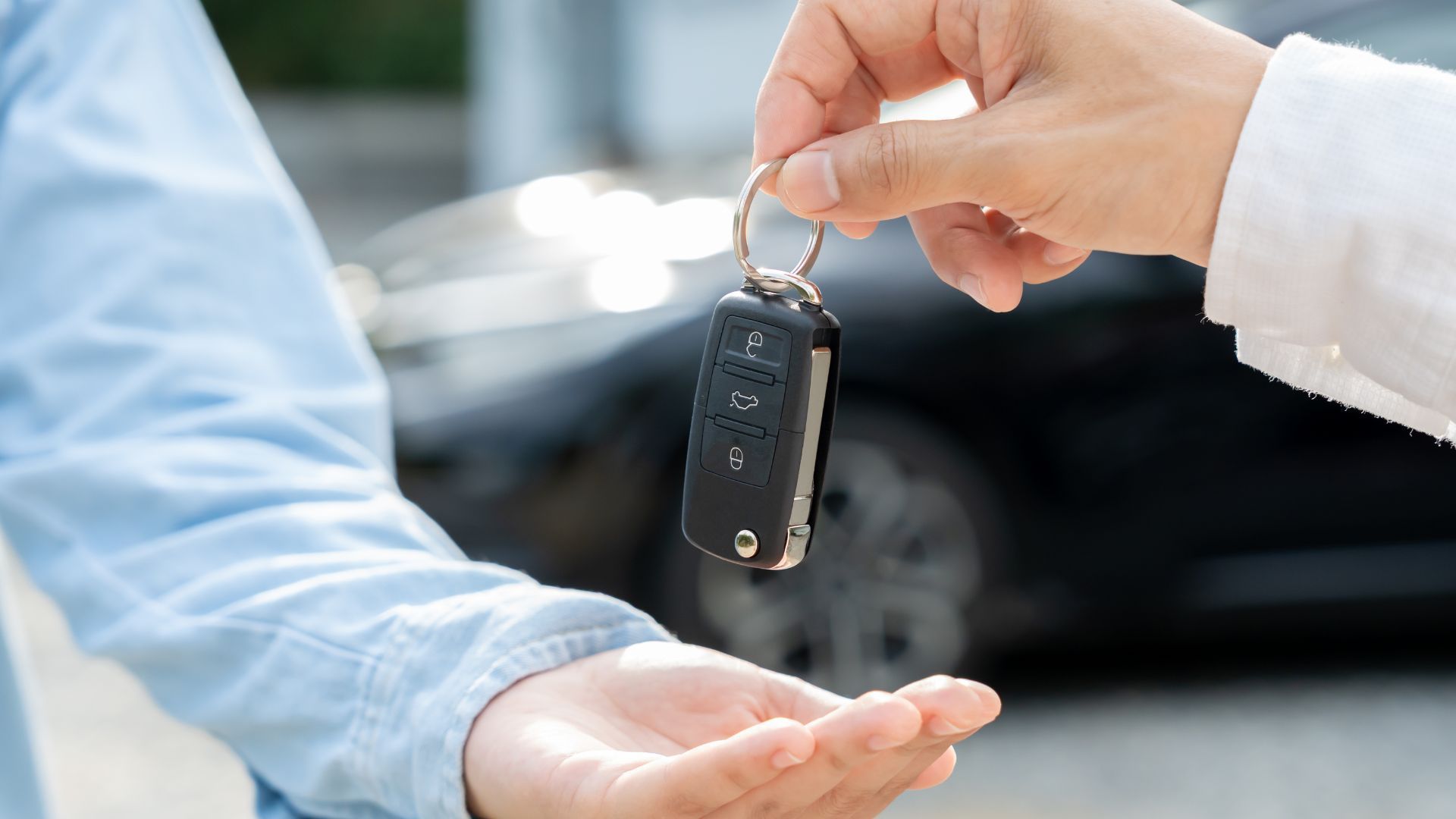 Handing over a car key in front of a parked vehicle