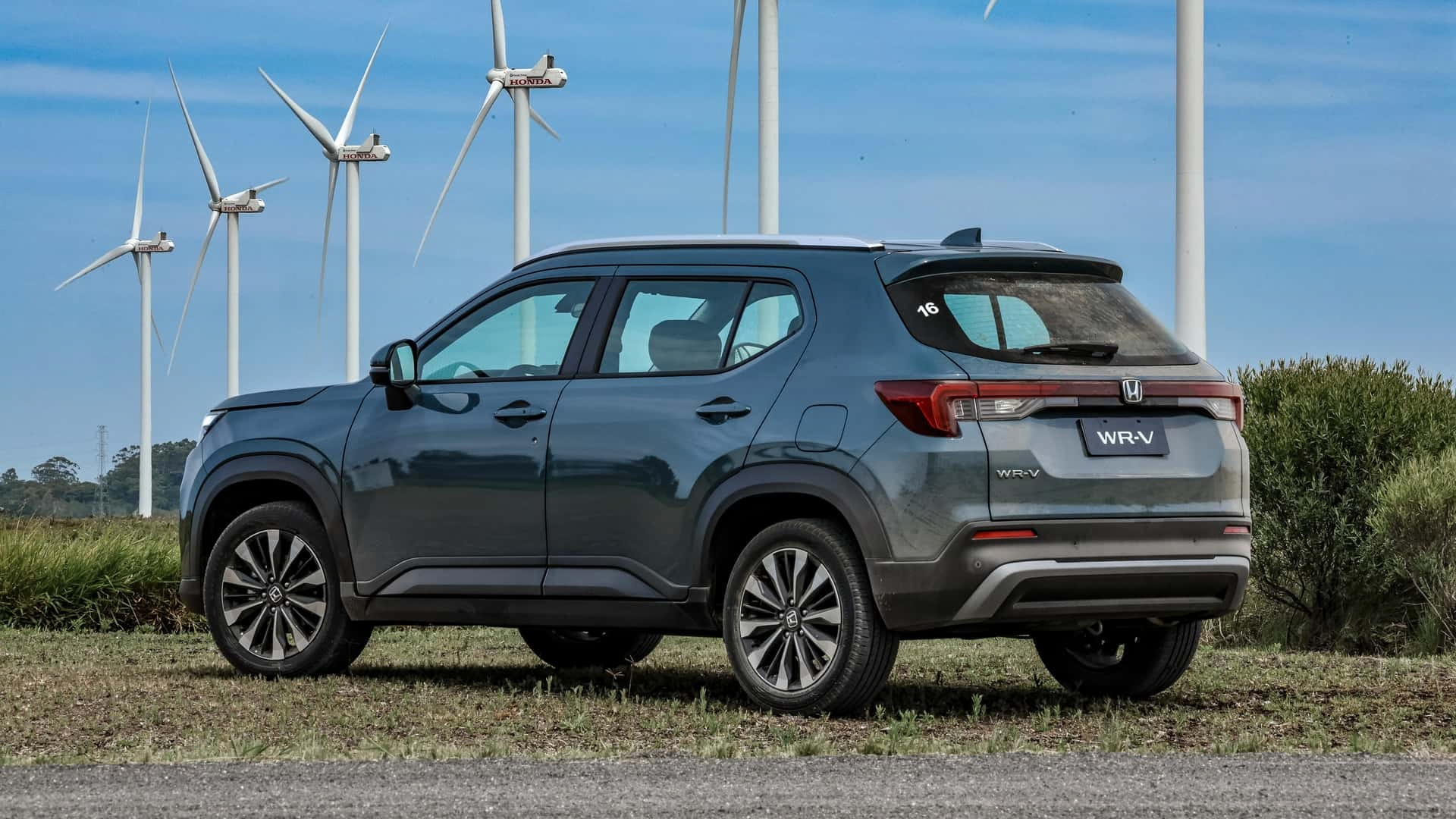 Gray SUV parked in a field with wind turbines in the background